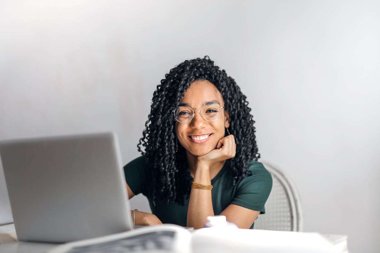 services-04 Joyful businesswoman with curly hair smiling at camera while using laptop indoors.