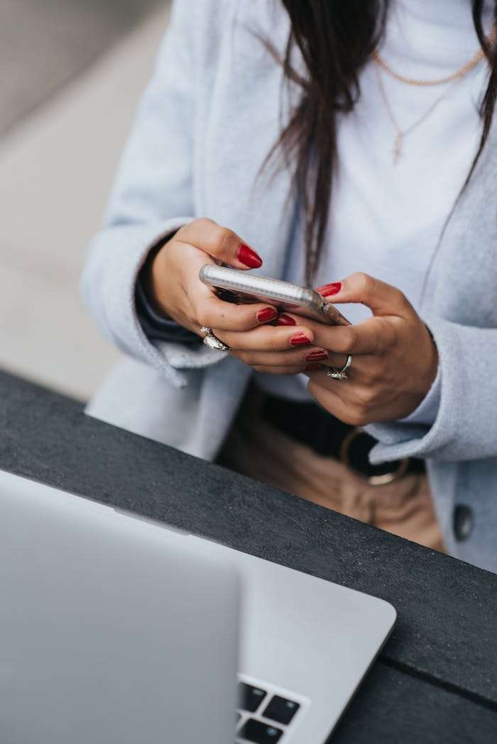 our-story A businesswoman with red nails using a smartphone outdoors next to a laptop.
